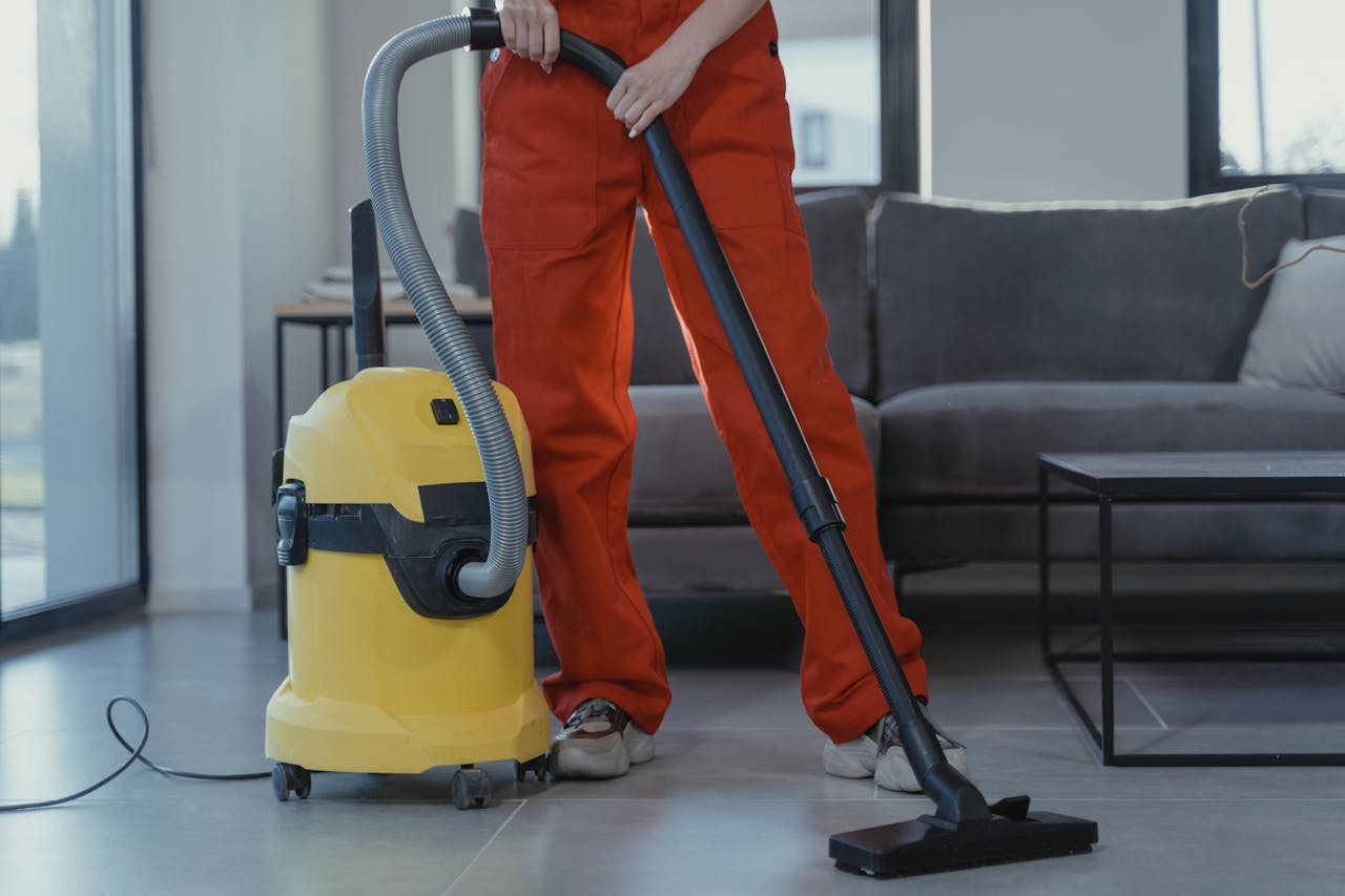 home-img A professional cleaner in red coveralls vacuums a contemporary living room with a yellow vacuum cleaner.